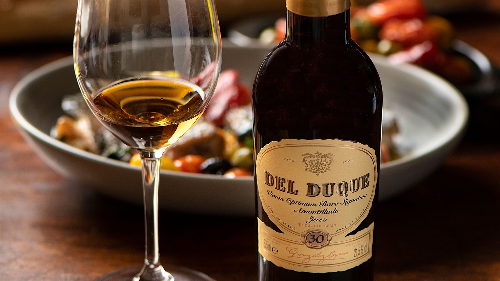A bottle and glass of Gonzalez Byass Del Duque 30 year, presented in front of a plate of olives.